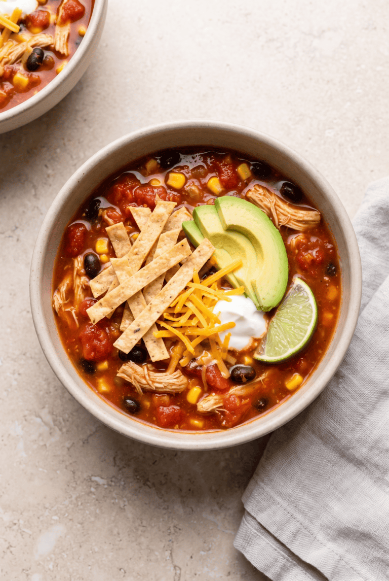 Bowl of crockpot chicken tortilla soup topped with tortilla strips and avocado