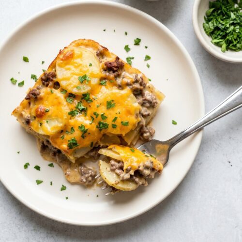 A square of hamburger potato casserole with sliced potatoes, ground beef, and cheddar in a creamy sauce