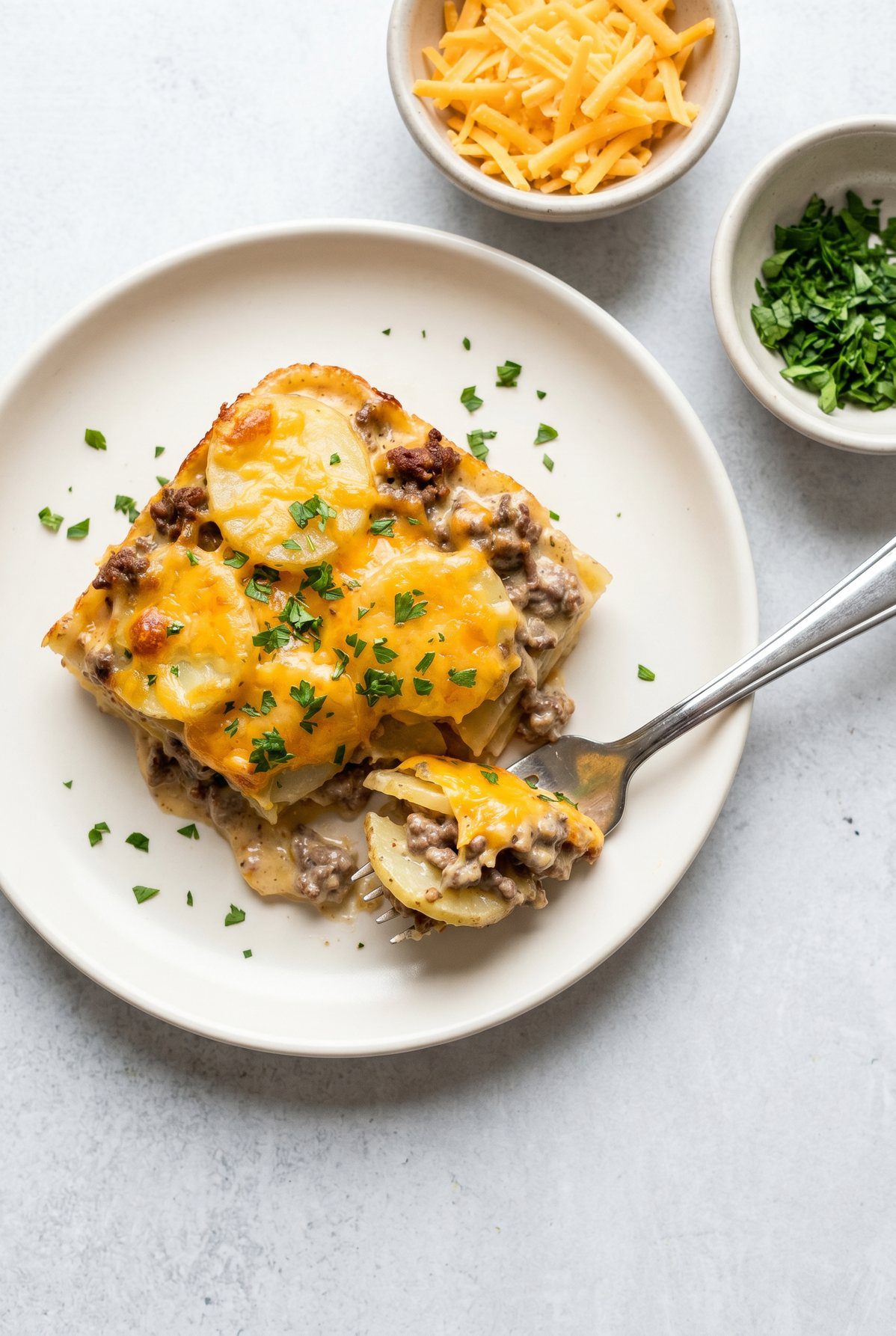 A square of hamburger potato casserole with sliced potatoes, ground beef, and cheddar in a creamy sauce