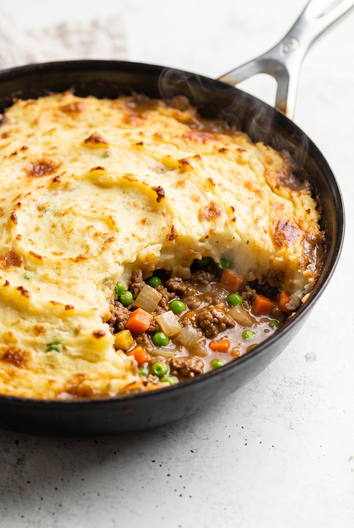 Shepherd's pie in a skillet with a browned mashed potato top over ground beef, peas, and carrots