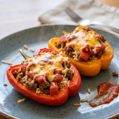 Two halved stuffed peppers filled with ground beef and rice, topped with tomato sauce and melted cheese
