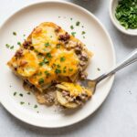 A square of hamburger potato casserole with sliced potatoes, ground beef, and cheddar in a creamy sauce